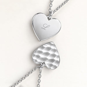 Close-up of two heart-shaped pendants in silver – rippled front and polished back with an engraved initial