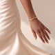 Model in a cream satin dress wearing a personalised gold bangle bracelet with an engraved date