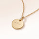 Close-up of a round gold pendant with a zirconia-set bail and personalised engraving of initials with a heart