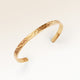 Close up af minimalistisk bangle armbånd i guld med bølget overflade og plads til personlig indgravering