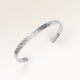 Close up af minimalistisk bangle armbånd i sølv med bølget overflade og plads til personlig indgravering