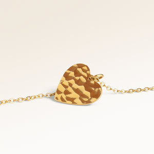 Close-up of minimalist heart-shaped heart pendant in gold with rippled wave surface and space for engraving on back
