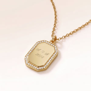 Close-up of an octagon gold pendant with white zirconia around the edge and a personal engraving of initials with a heart and a year